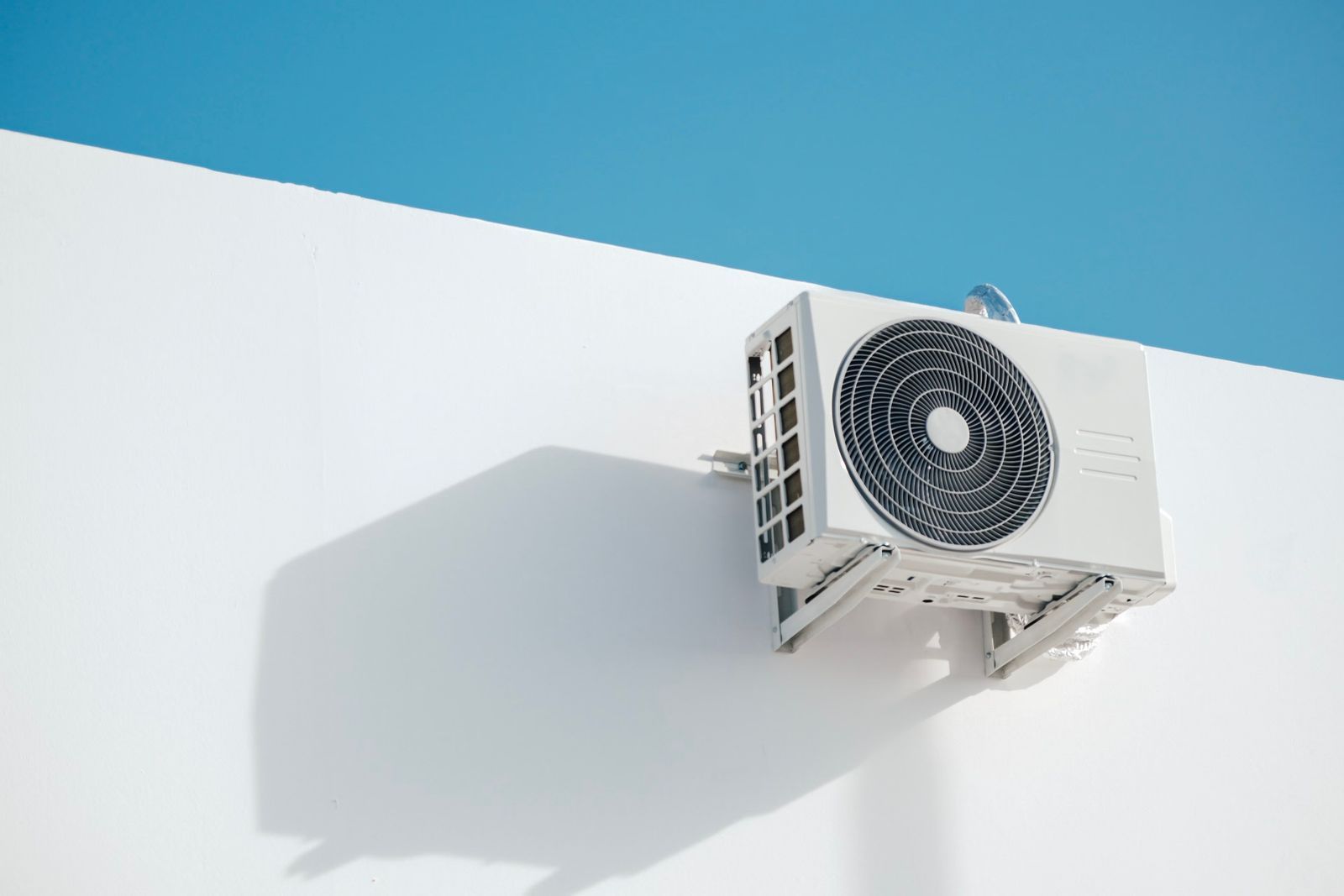 Unité extérieure de pompe à chaleur sur un mur blanc, ciel bleu